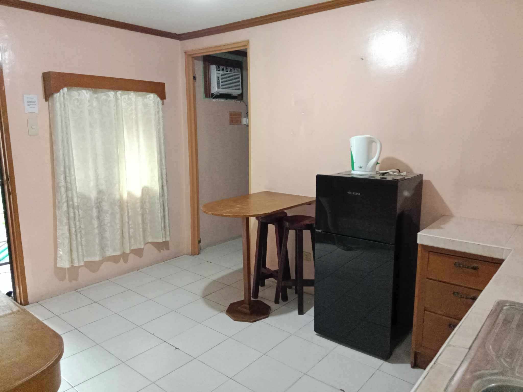 A compact kitchen with a refrigerator, a wooden table, and a single stool.