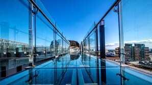 Una piscina de vidrio moderna con vista infinita al paisaje urbano y una montaña distante.