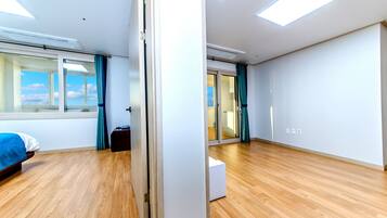 Una habitación de hotel moderna con suelo de madera, una cama, un ventanal grande con cortinas y una puerta corredera que da a otra habitación.