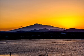 Un atardecer sobre una masa de agua, con una montaña al fondo y aerogeneradores.