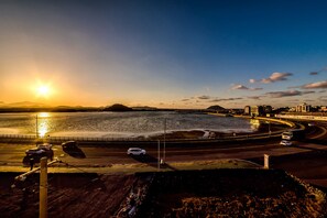 Una strada costiera con un tramonto, un ponte e uno skyline cittadino sullo sfondo.