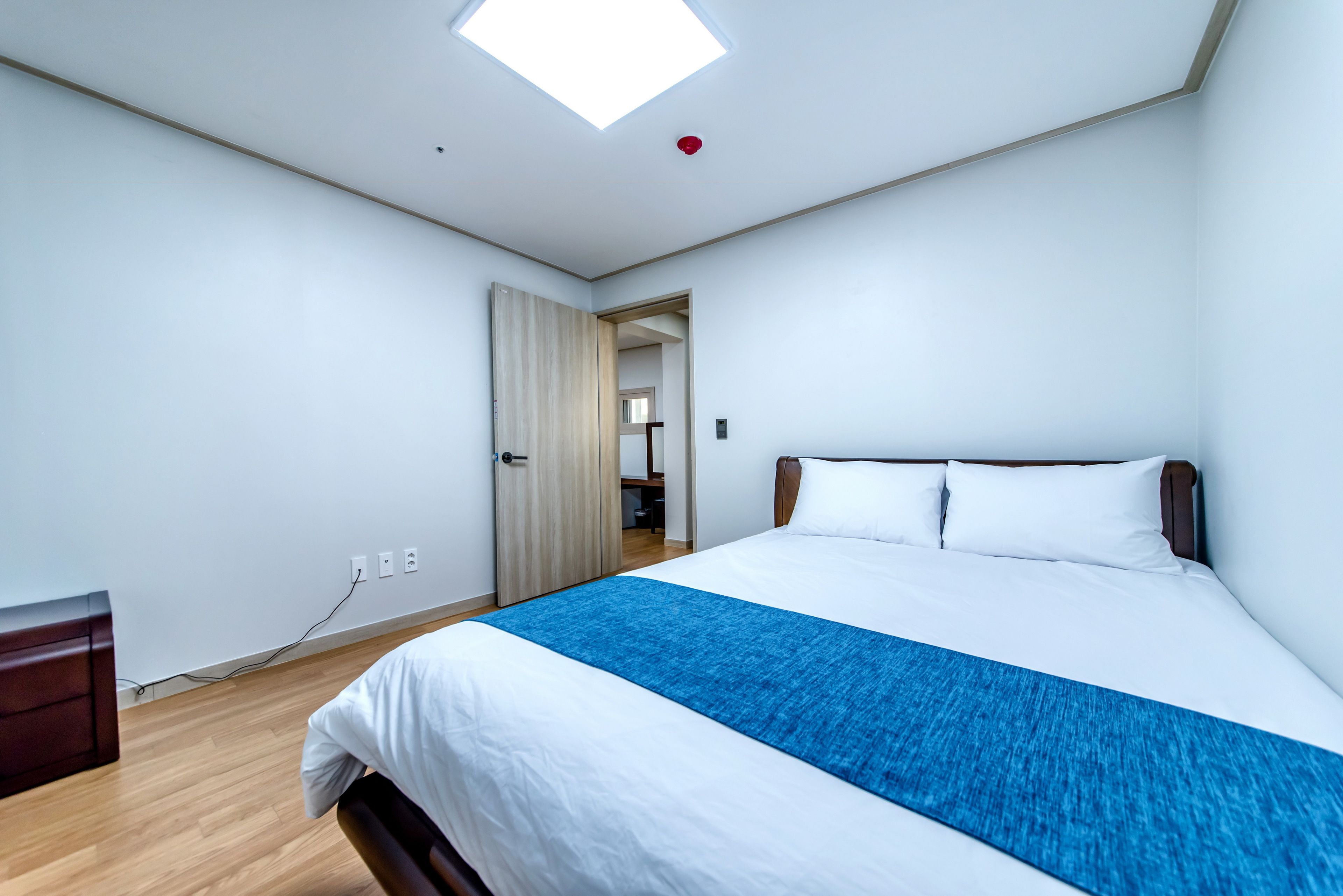 Una habitación de hotel moderna con una cama grande, una mesita de noche de madera, un escritorio y un tragaluz.