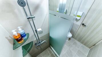 A modern bathroom with a glass shower enclosure, a handheld showerhead, and a shelf with soap dispensers.