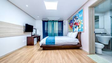 A modern hotel room with a wooden floor, a large bed with white bedding, a flat-screen TV mounted on the wall, a painting above the bed, and a bathroom with a toilet and sink.