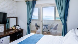 Habitación de hotel con cama, televisor, escritorio con tetera y balcón con sillas.