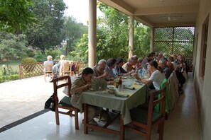 A covered outdoor dining area with tables and chairs, surrounded by greenery and a fence. - Hotel Parkland (Sauraha)