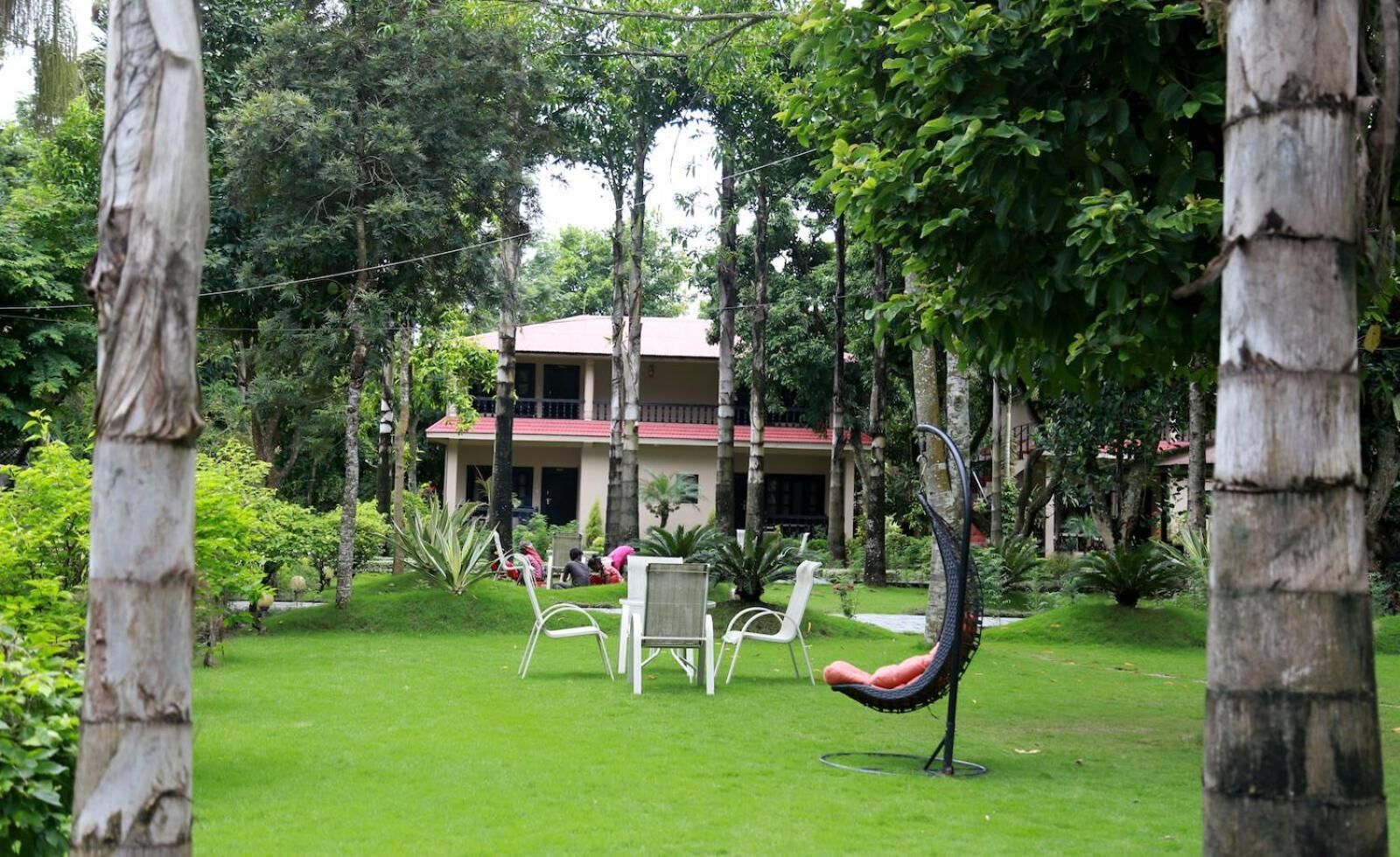 A lush garden with a building in the background, surrounded by trees and greenery.