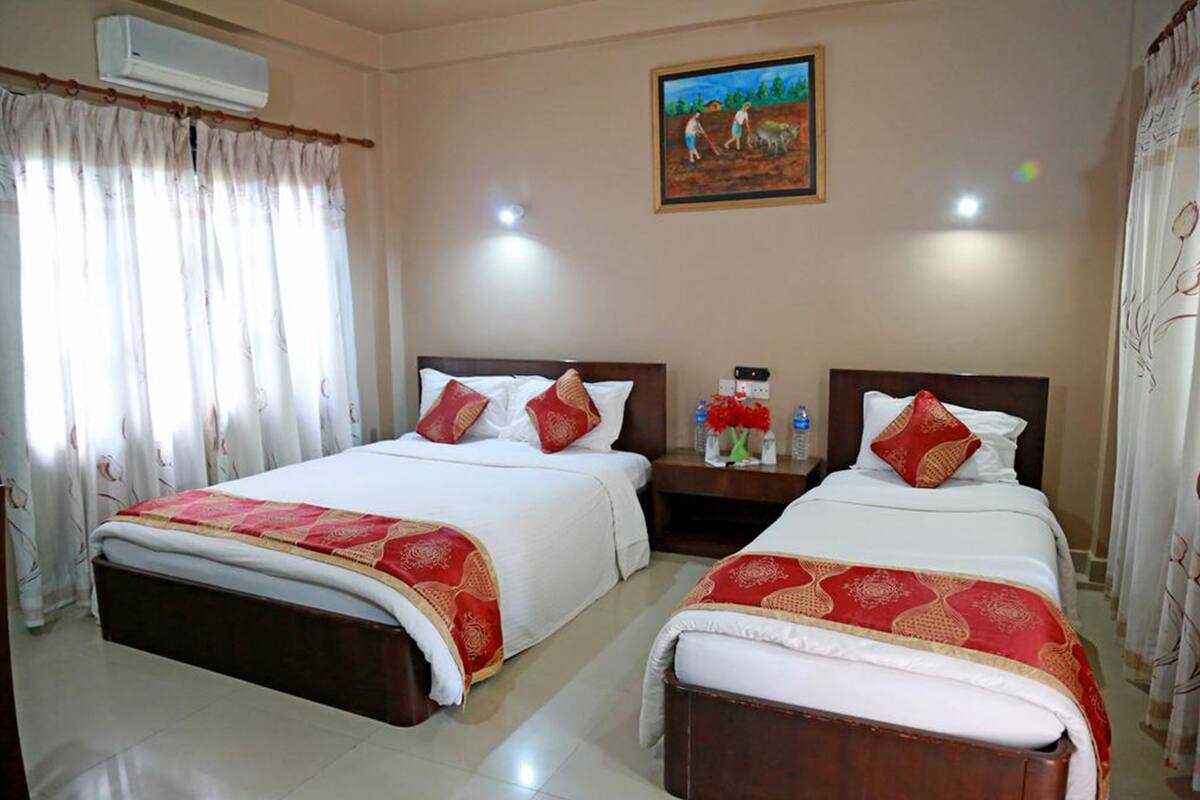 A hotel room with two beds, each with a red and white bedspread, a nightstand with a vase of flowers, and a painting on the wall.