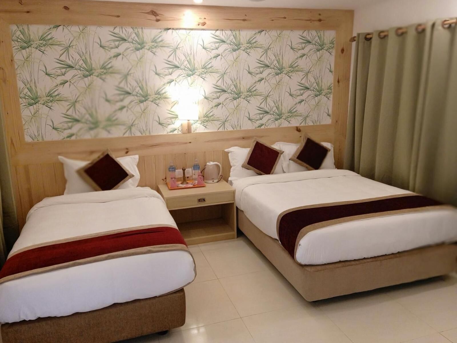 A hotel room with two beds, a wooden headboard, a nightstand with a lamp, and a wall with a bamboo pattern.