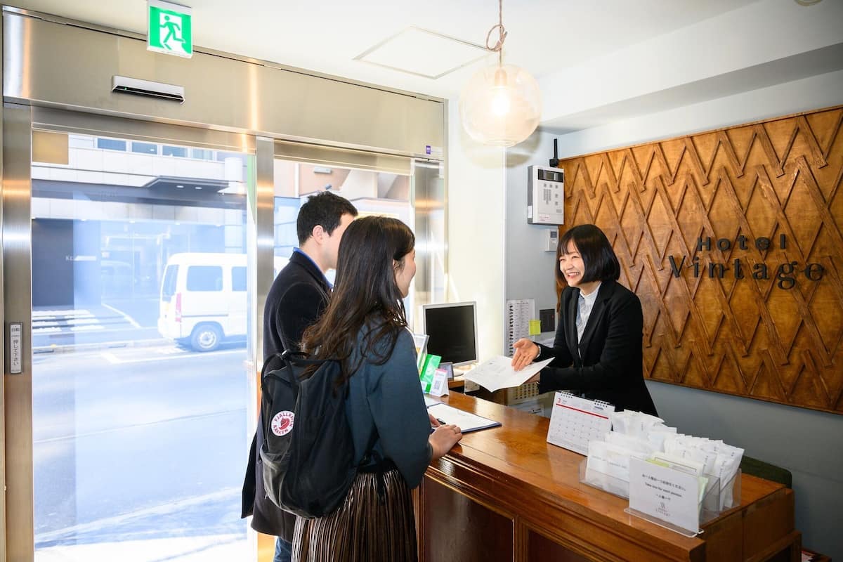 A reception desk with a wooden wall, a sign reading 'Hotel Vintage,' and a view of a street outside.