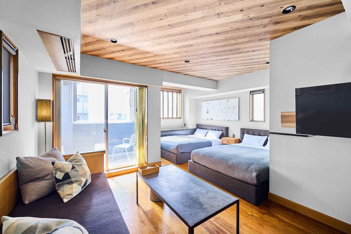 A modern room with a wooden ceiling, a sofa, a bed, a TV, and a sliding glass door.