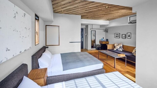 Habitación de hotel moderna con una cama grande, un sofá, un escritorio y techo de madera.