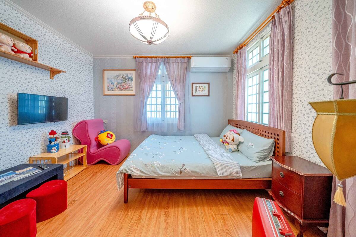 A bedroom with a wooden bed, a desk with a chair, a television, and a window with curtains.