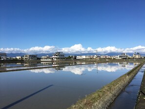 Un paisaje sereno con cielo despejado, agua tranquila que refleja edificios y montañas distantes.