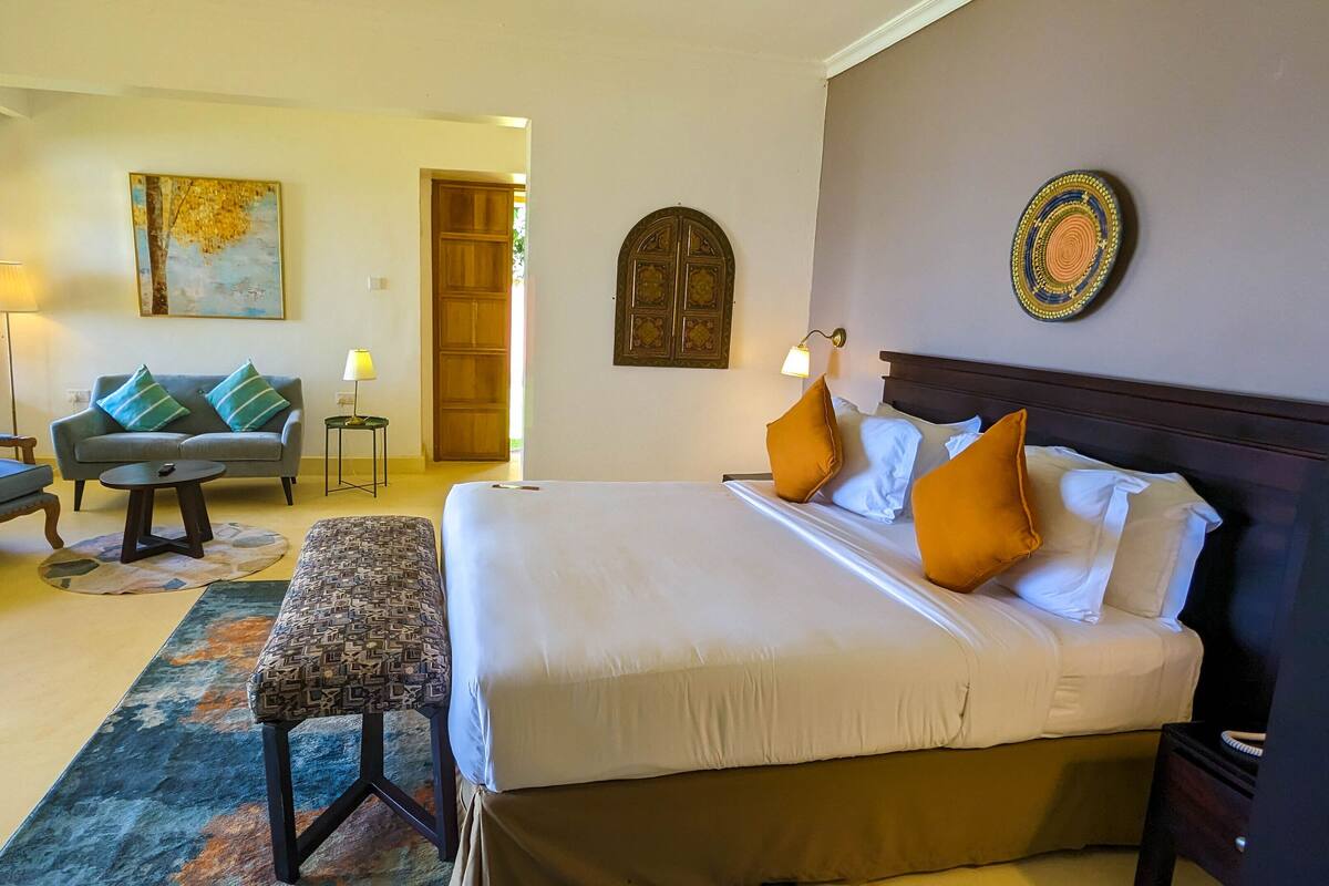 Una habitación de hotel con una cama grande, un sofá, una silla, una mesita y una lámpara.