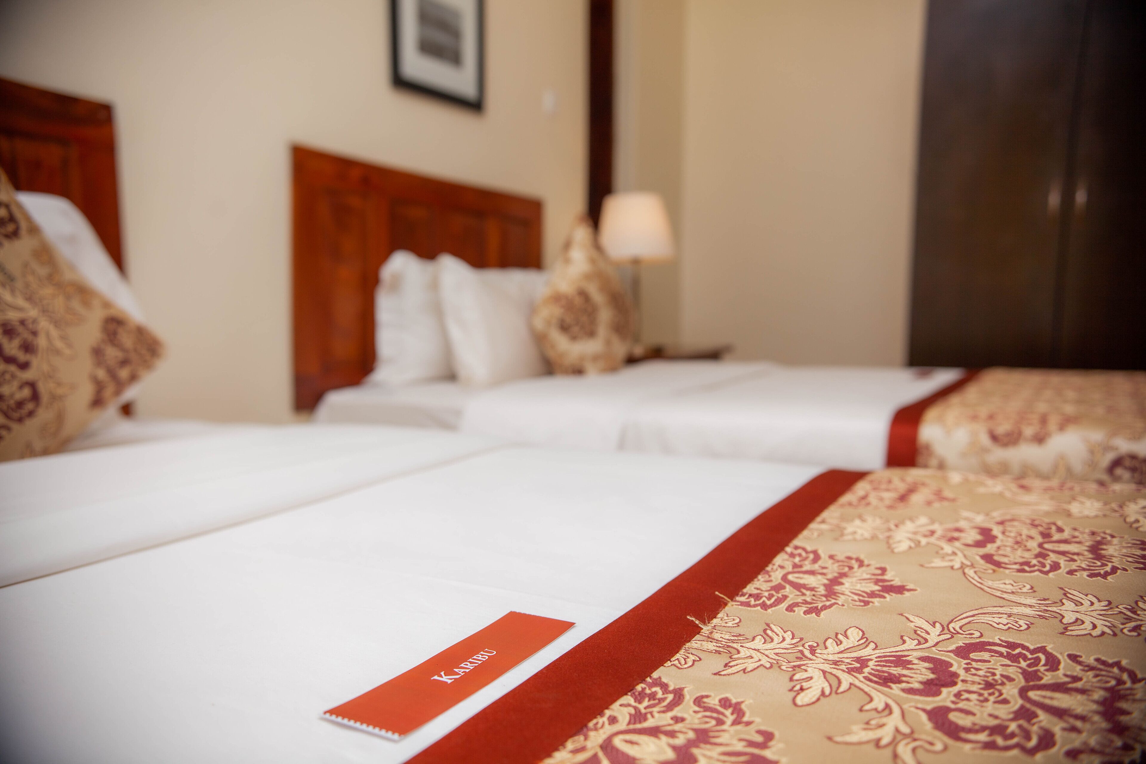 A hotel room with two beds, a wooden headboard, a nightstand with a lamp, and a framed picture on the wall.