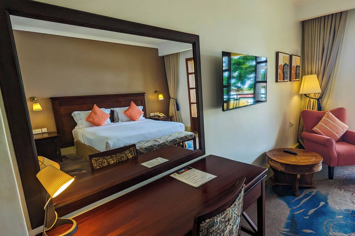 Habitación de hotel con cama, escritorio, silla, televisor y ventana con cortinas.