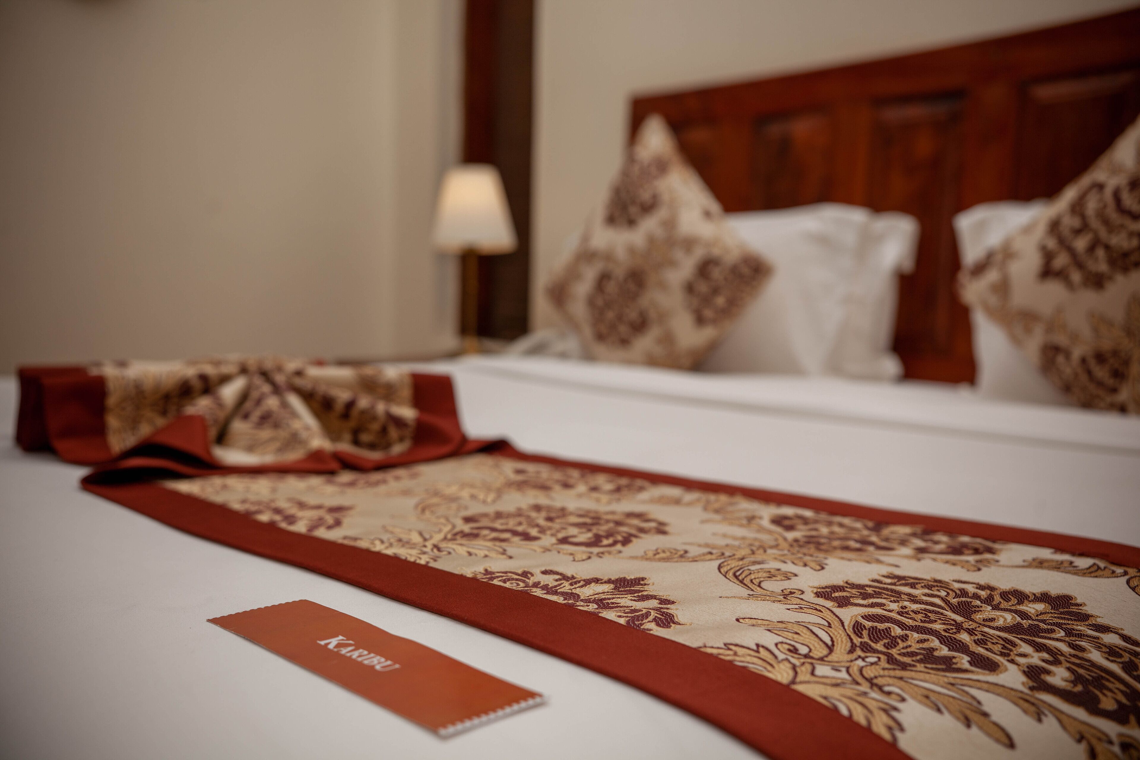 Una cama bien hecha con un corredor rojo y beige, una almohada blanca y una tarjeta roja sobre la cama.