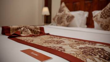 Una cama bien hecha con un corredor rojo y beige, una almohada blanca y una tarjeta roja sobre la cama.
