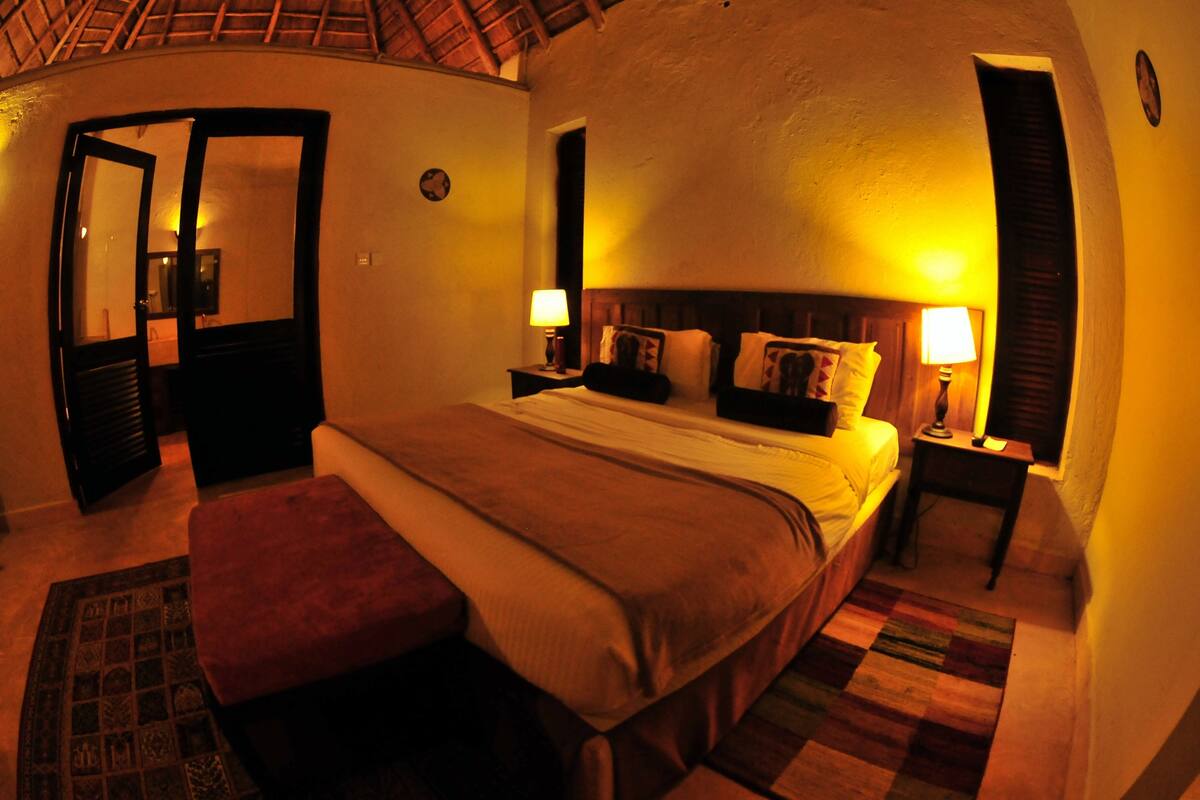 Un dormitorio con cama, mesitas de noche, un velador, un espejo y una puerta.