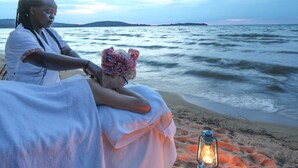 Una persona seduta su una sedia da spiaggia con un asciugamano, vicino a una lanterna sulla sabbia.