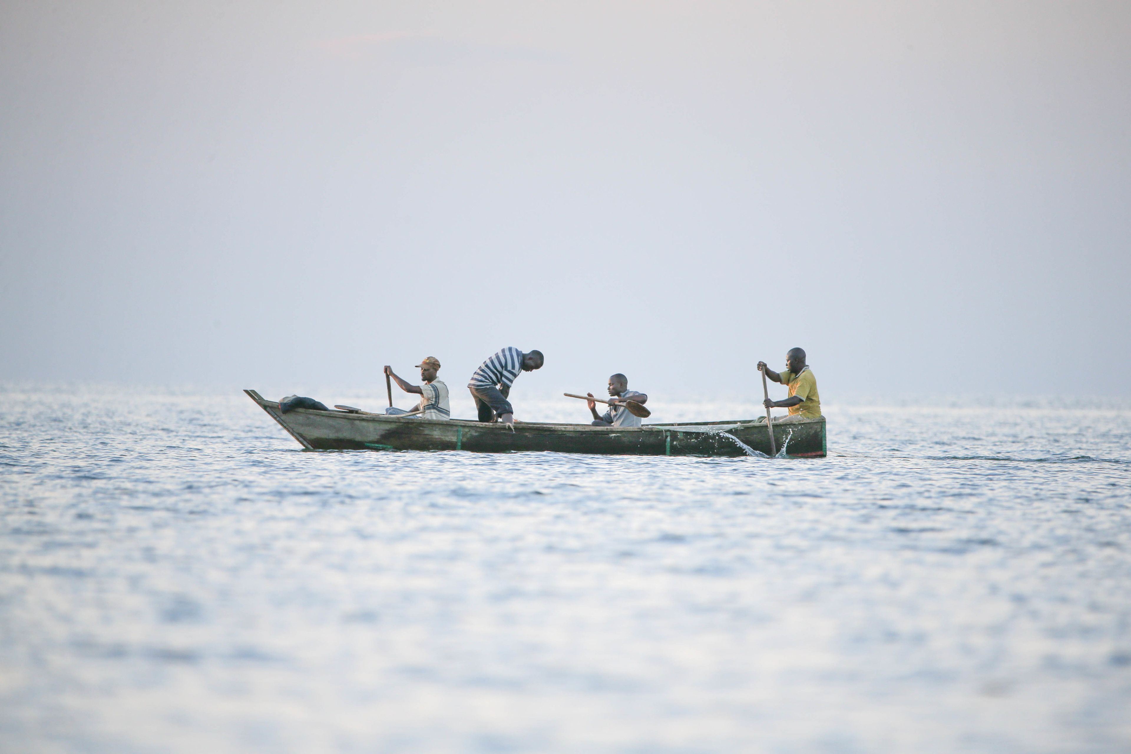 Un bote pequeño con cuatro personas remando en un mar tranquilo.
