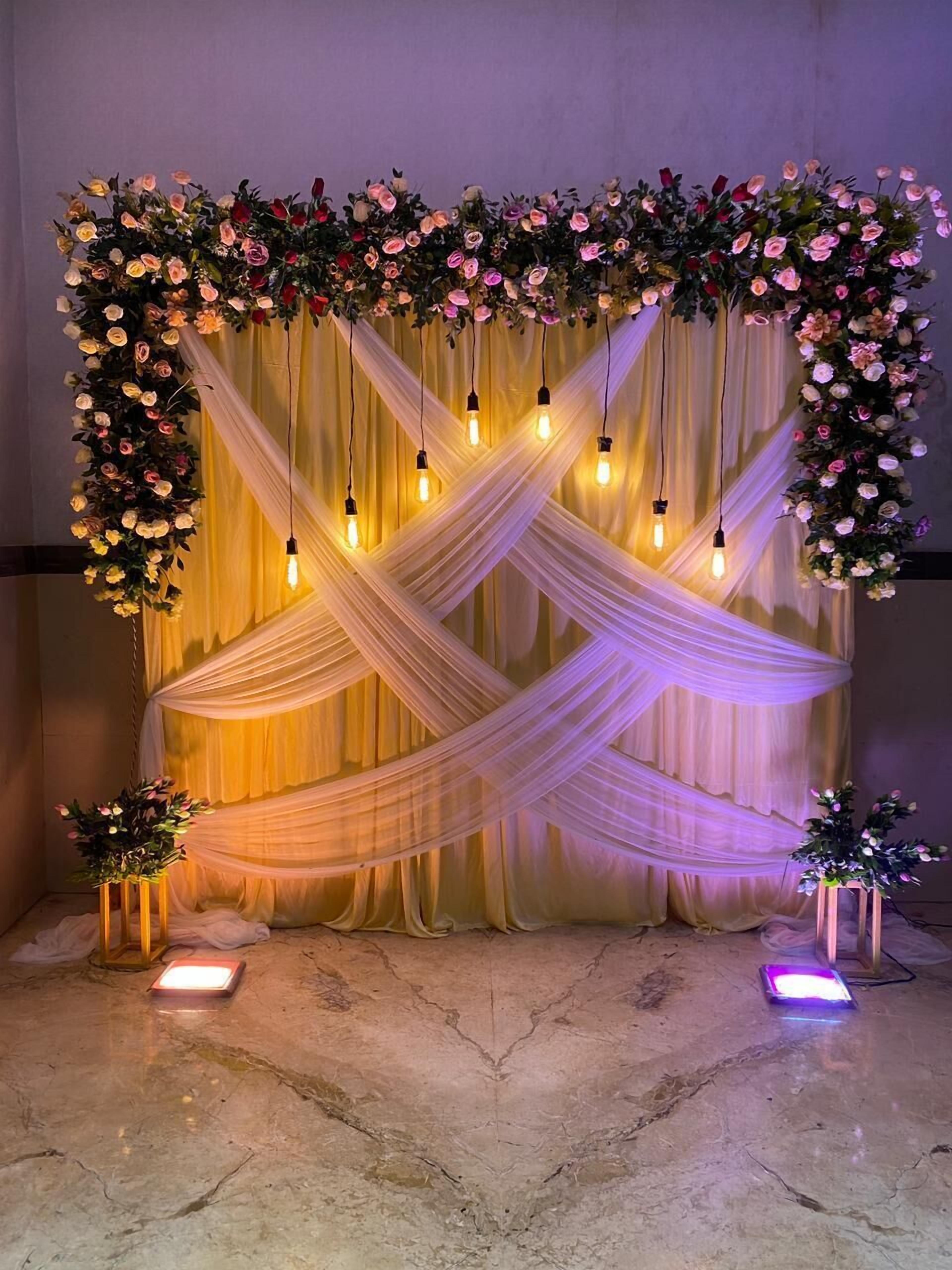 Eine Bühne mit Stoffvorhängen und floralen Dekorationen, beleuchtet durch hängende Lichter.