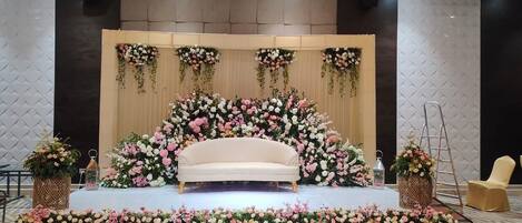 A stage with a sofa, surrounded by floral arrangements and a wooden backdrop.