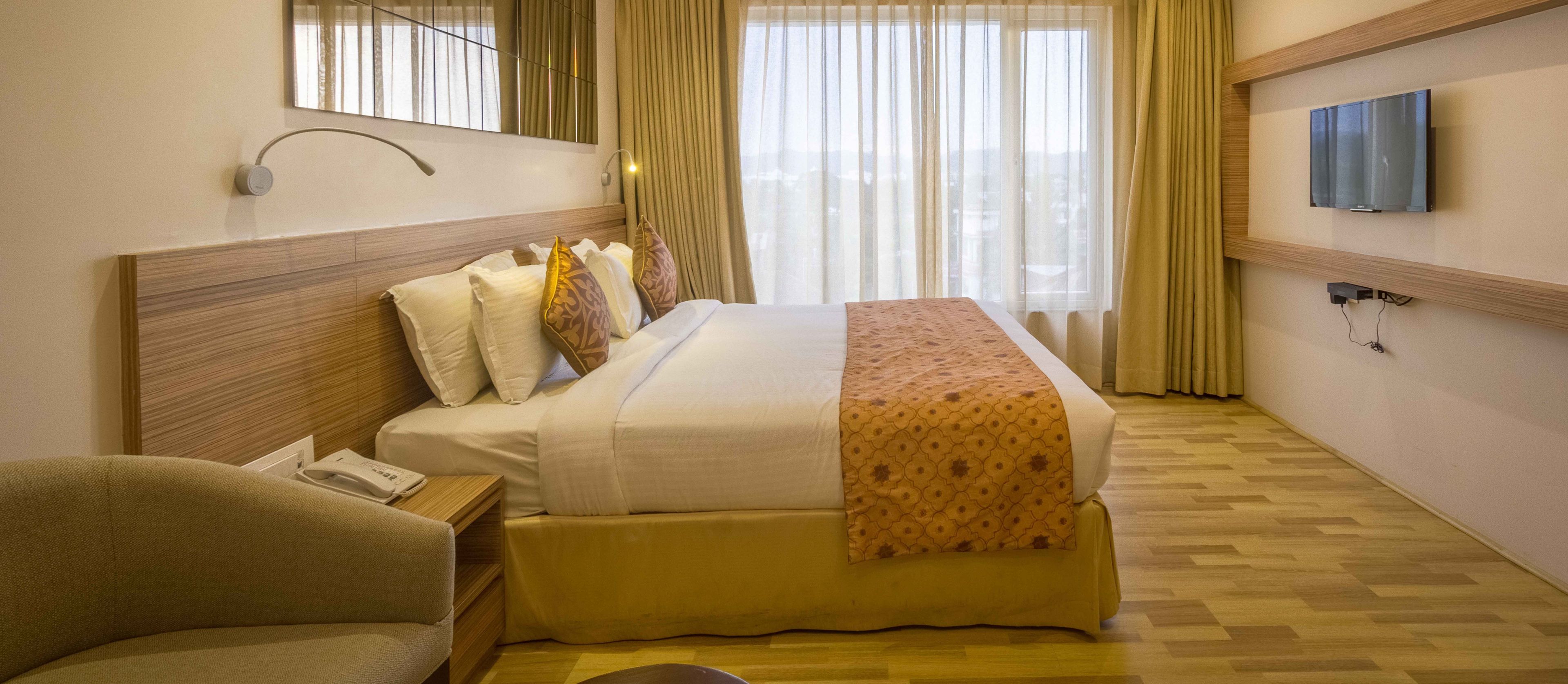 A hotel room with a bed, a chair, a TV, and a window with curtains.