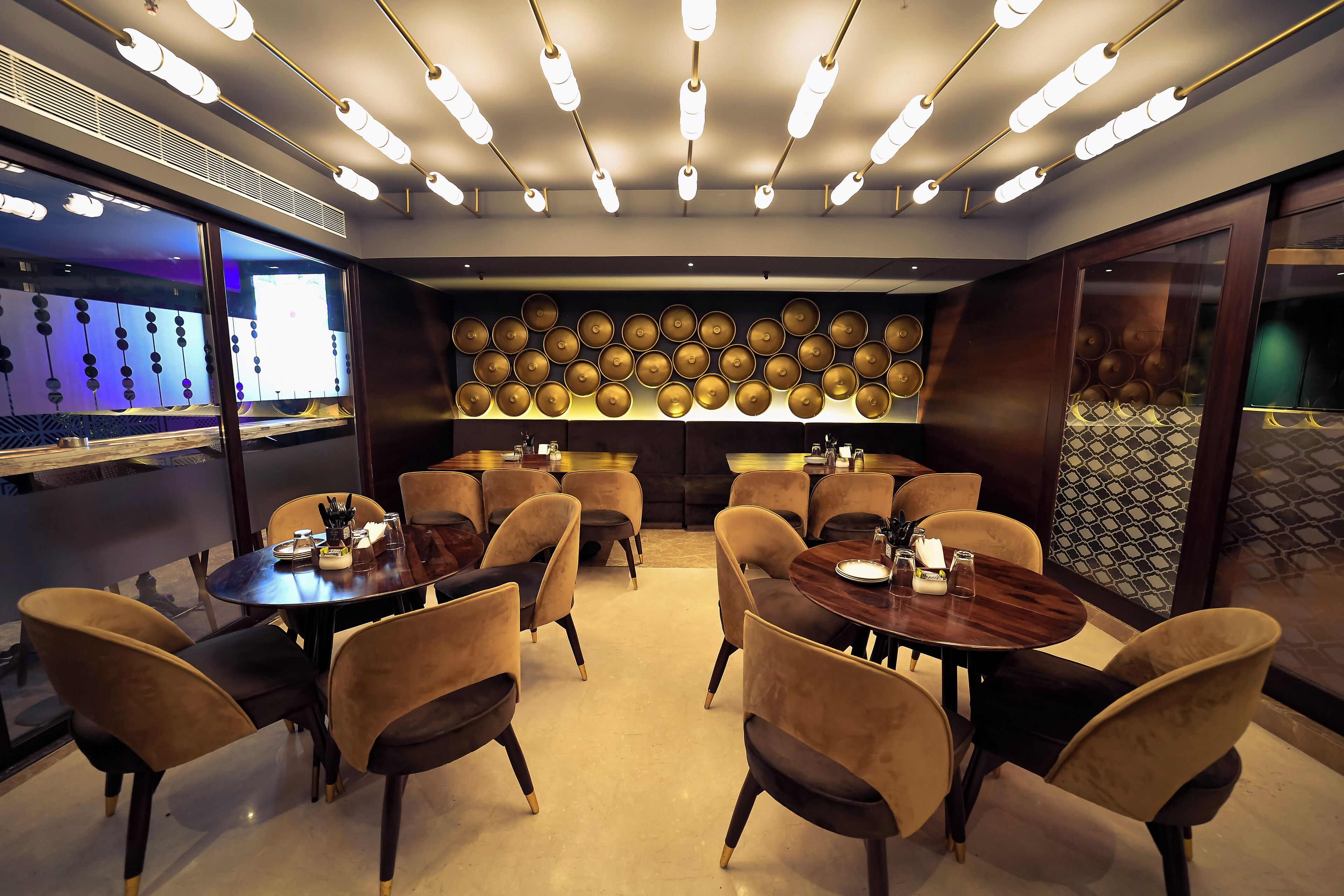 A modern dining area with round tables and chairs, overhead lighting, and decorative wall panels.