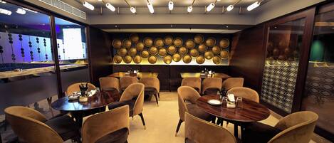 A modern dining area with round tables and chairs, overhead lighting, and decorative wall panels.