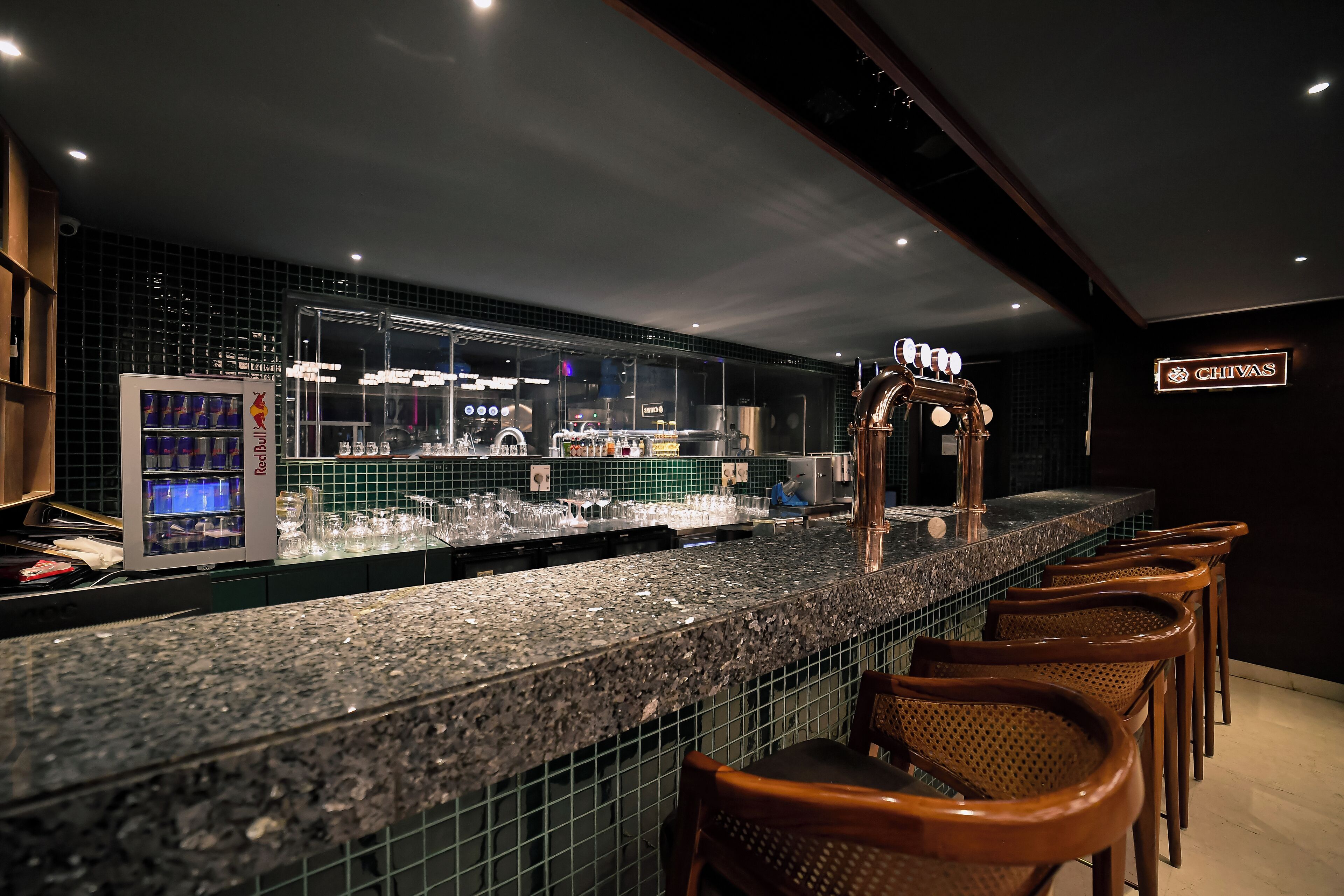 A bar area with a granite countertop, bar stools, and a refrigerated display case.