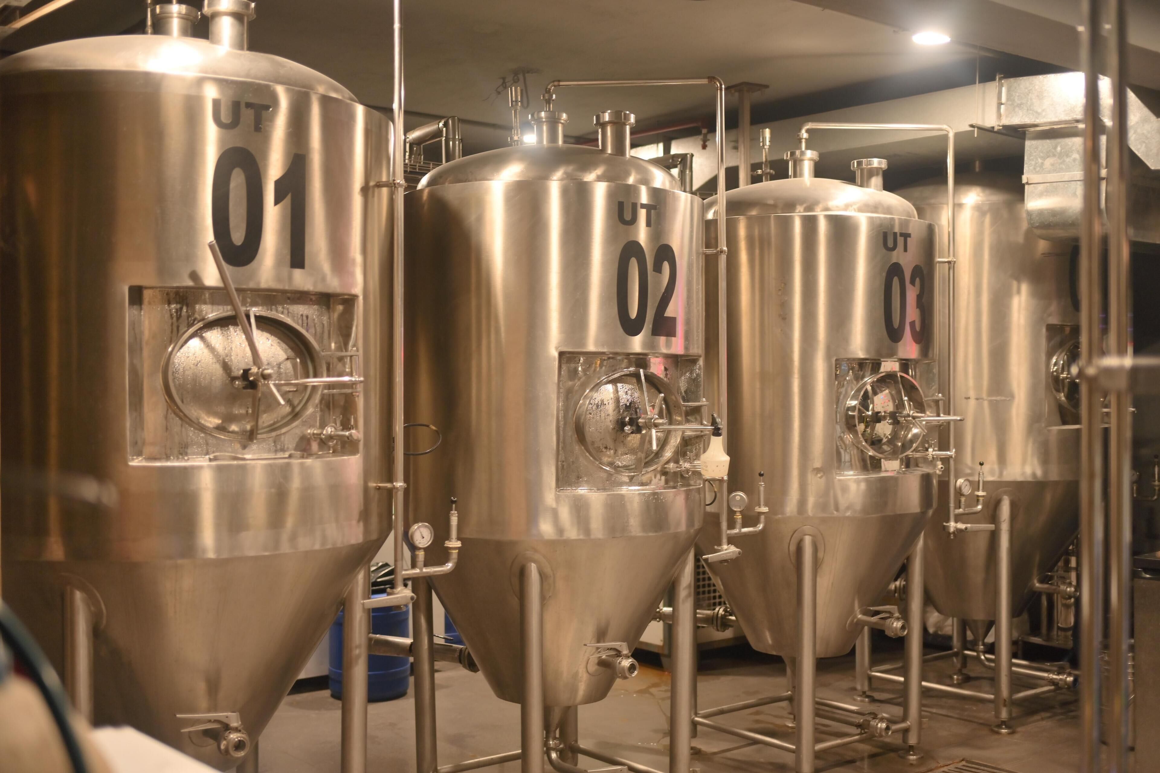 Stainless steel fermentation tanks labeled 01, 02, and 03 in a brewery setting.