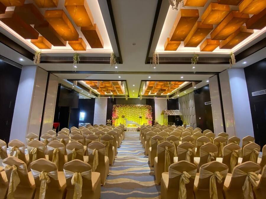 Salão de banquetes com fileiras de cadeiras e palco decorado com flores.