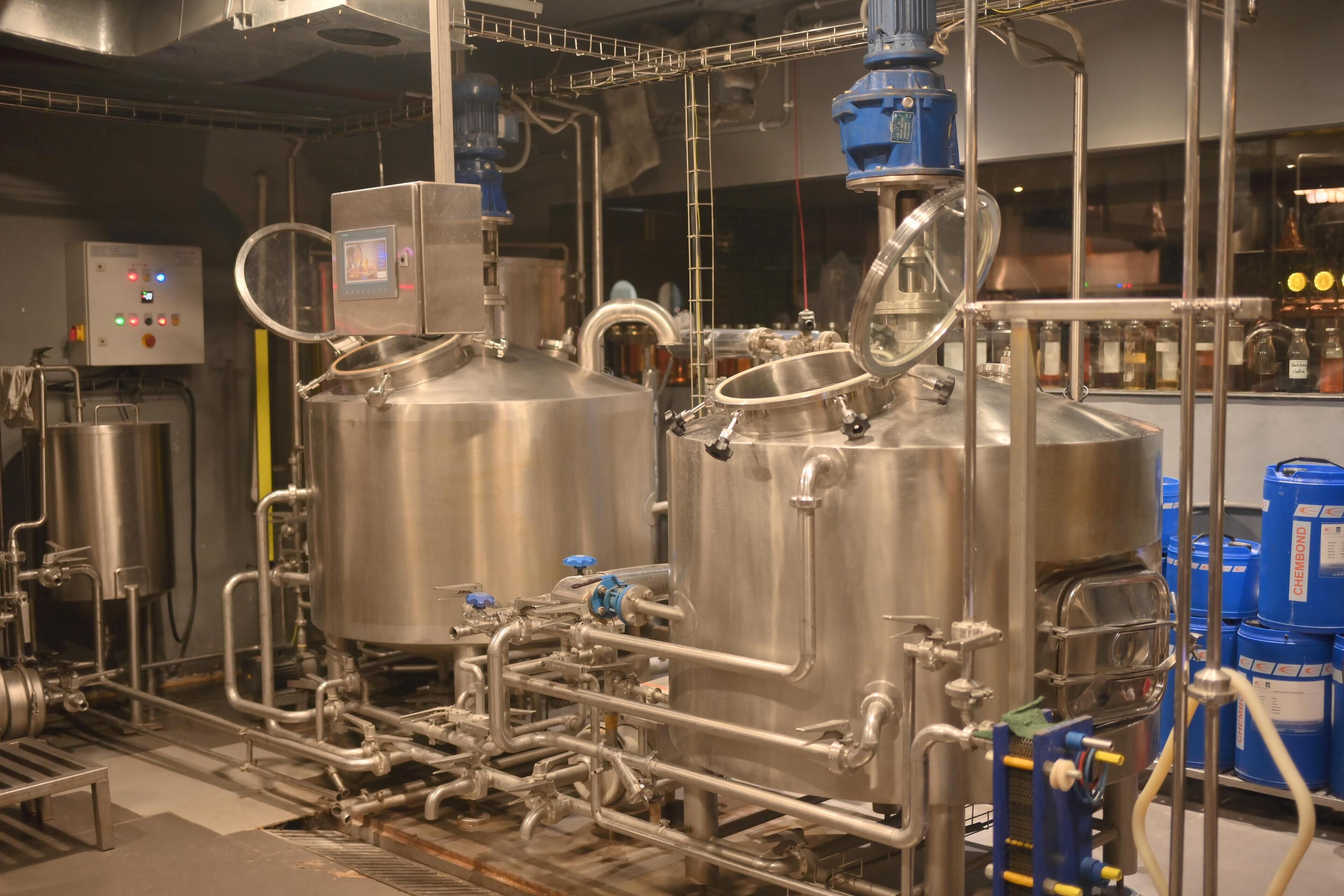 A stainless steel industrial kitchen with large cooking vessels, complex piping, and a control panel.