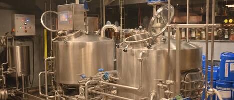 A stainless steel industrial kitchen with large cooking vessels, complex piping, and a control panel.