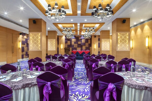 A banquet hall with rows of tables, purple chairs, and chandeliers. - Hotel Palacio (Guwahati)