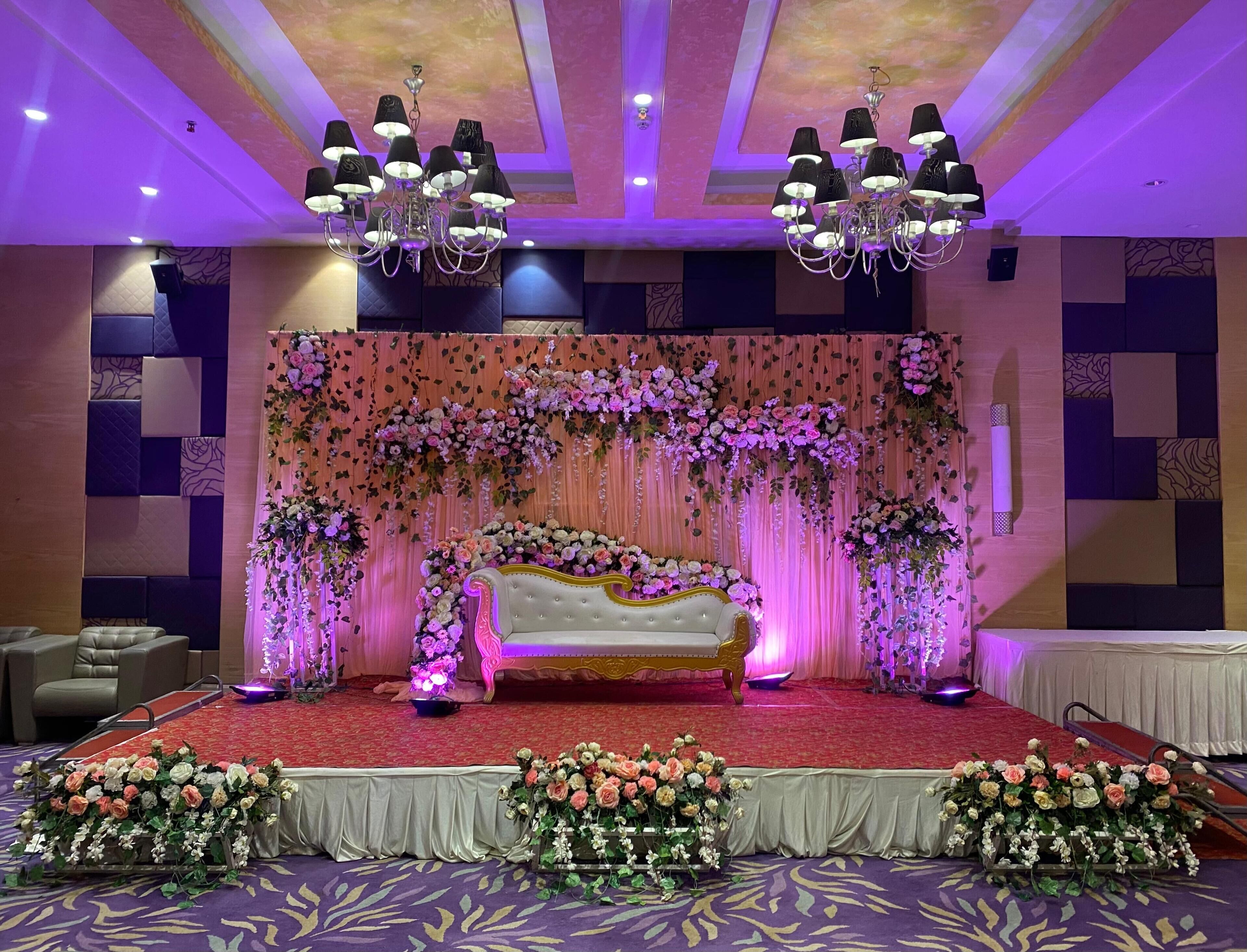 A stage with a sofa, floral arrangements, and chandeliers.