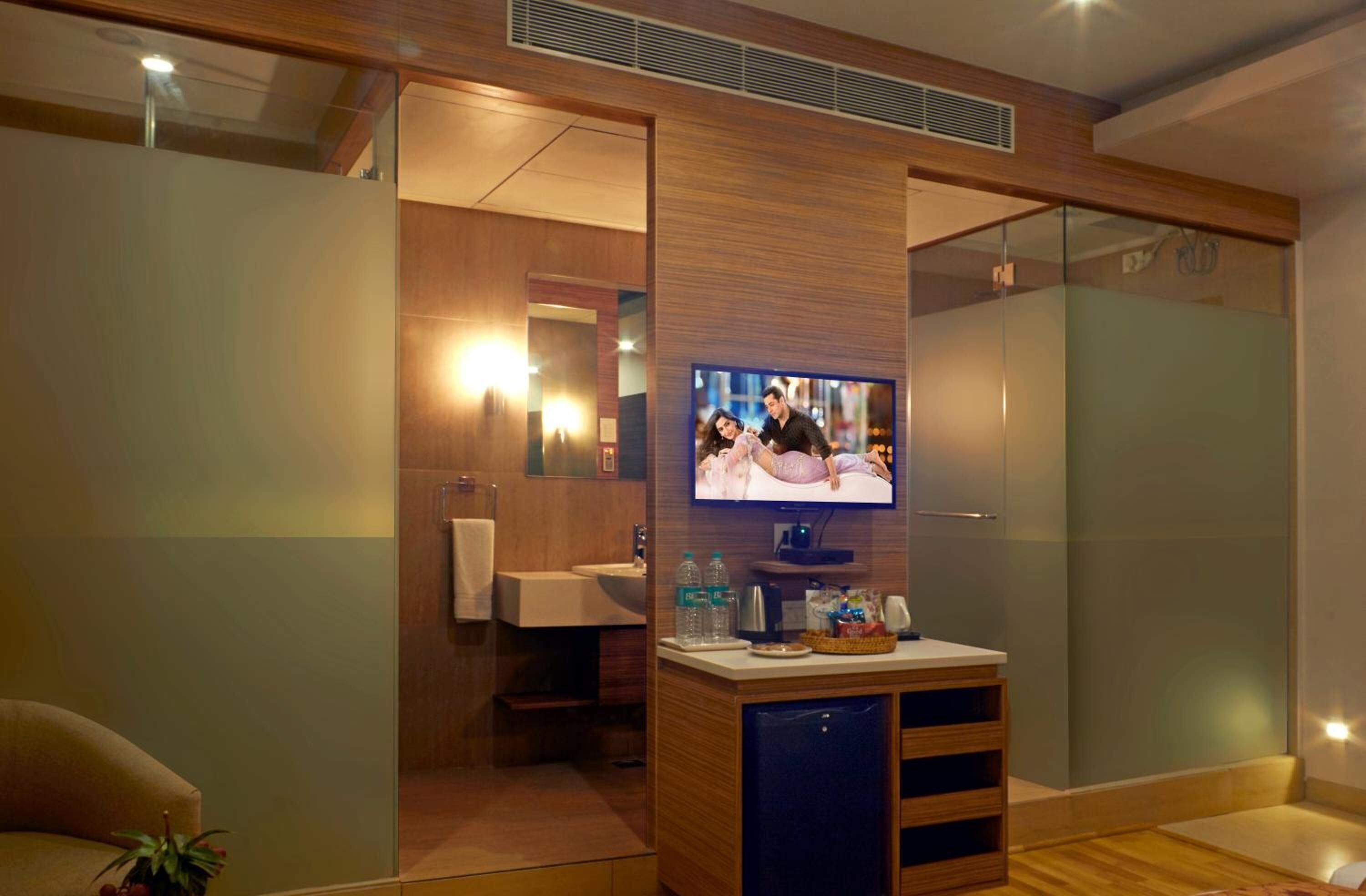 A modern bathroom with a glass shower, a vanity with a mirror, and a television mounted on a wooden panel.