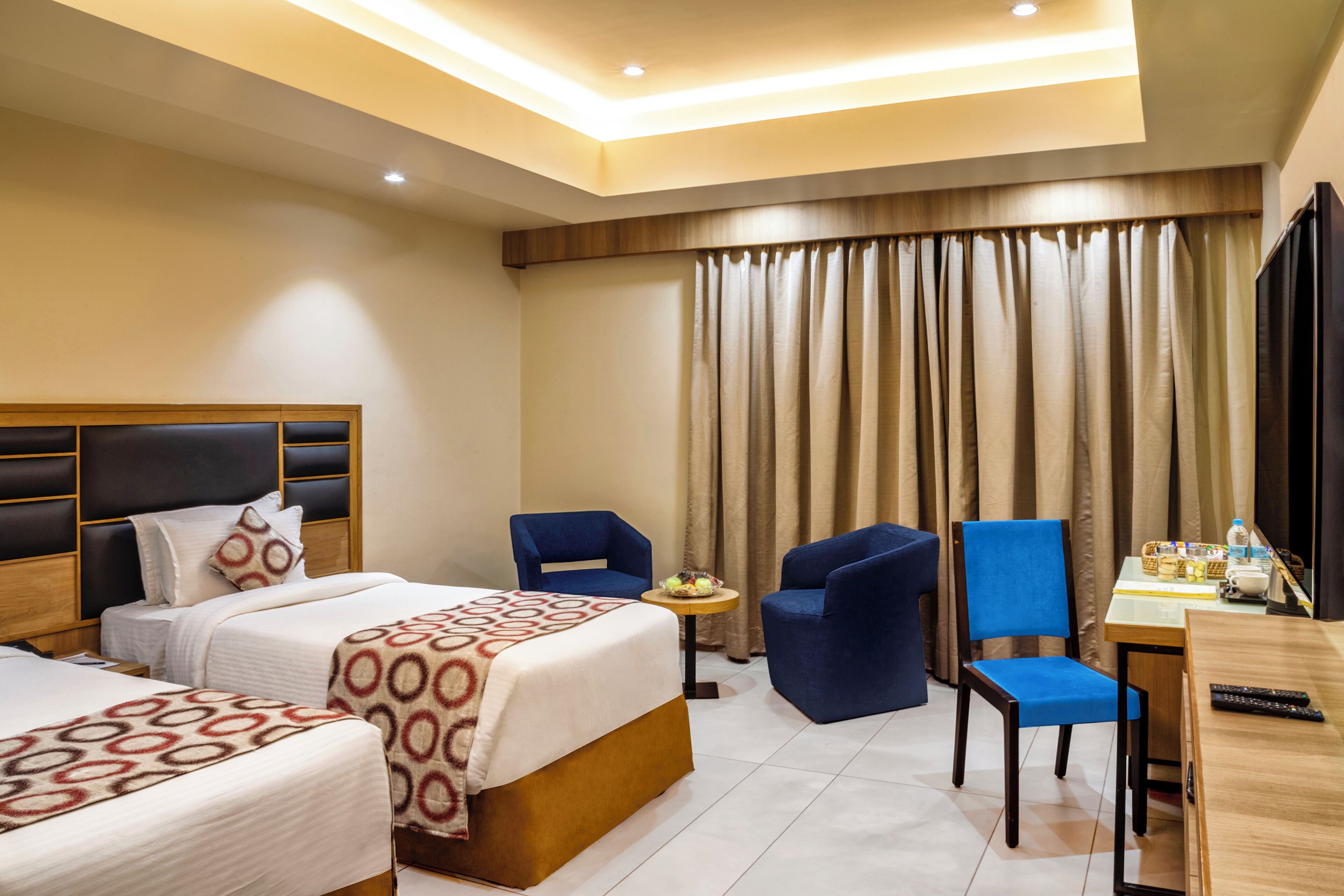 A hotel room with two beds, a desk, and two blue chairs.