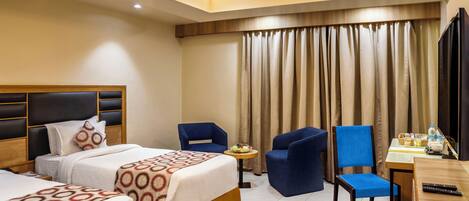 A hotel room with two beds, a desk, and two blue chairs.