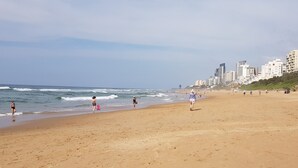 A beach with people walking and playing, a clear sky, and buildings in the background. - Crooked Tree Cottage (Umhlanga)