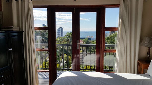 A bedroom with a large sliding glass door leading to a balcony with a city view. - Crooked Tree Cottage (Umhlanga)