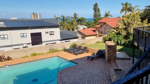 A residential area with a swimming pool, lounge chairs, and a view of the ocean. - Crooked Tree Cottage (Umhlanga)