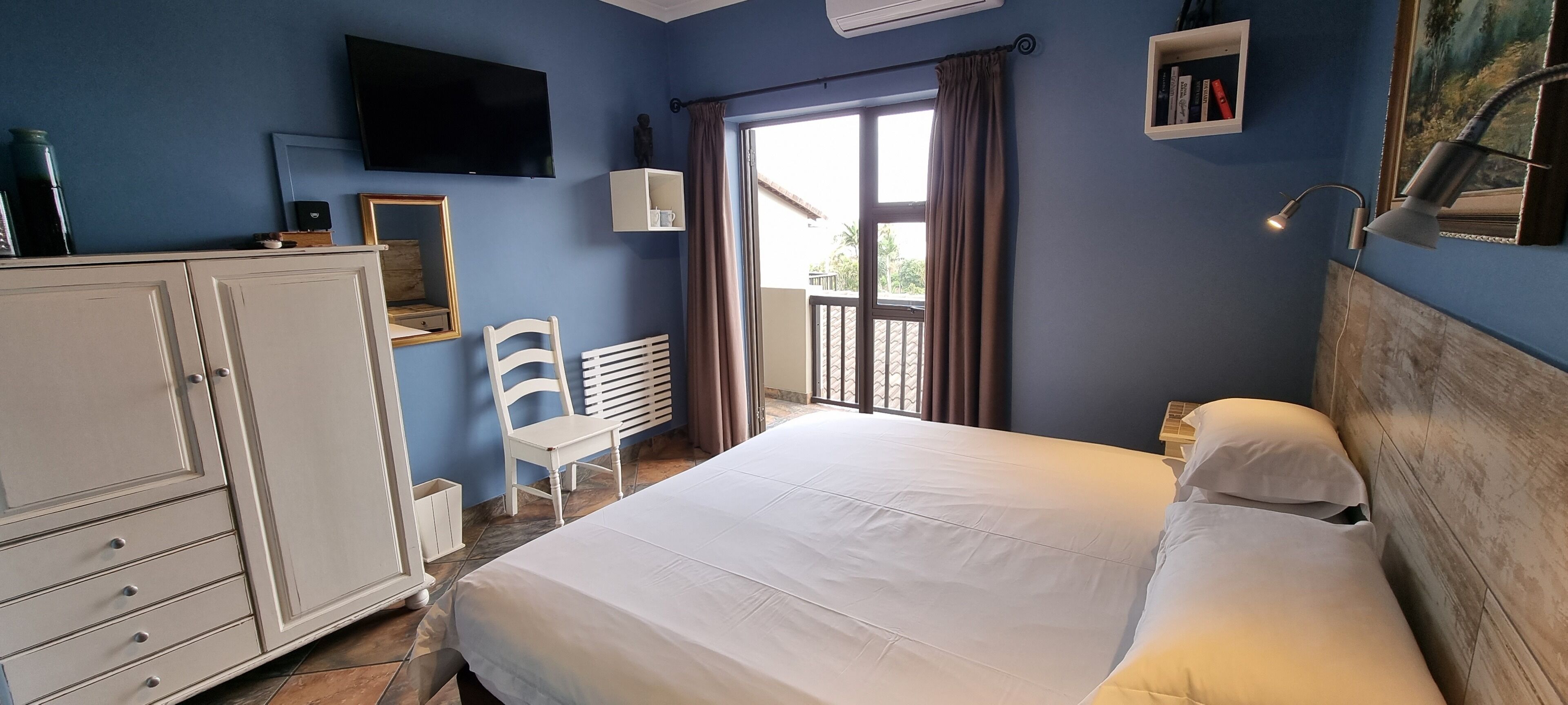 Un dormitorio con cama, armario, silla, televisor y ventana con cortinas.