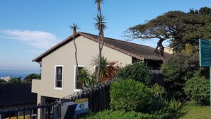 A two-story house with a tiled roof, surrounded by lush greenery and a view of the ocean. - Crooked Tree Cottage (Umhlanga)
