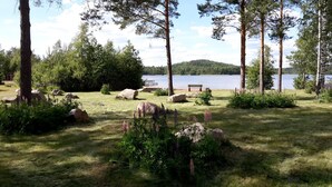 Un parc paisible au bord d’un lac, avec un banc en bois, de gros rochers et une végétation luxuriante.