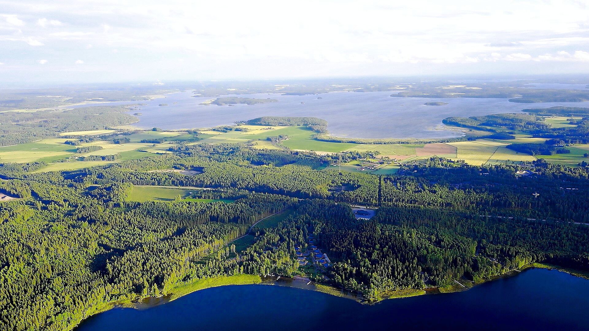 Une vue aérienne d’une zone côtière avec de vastes forêts, un lac et quelques bâtiments dispersés.