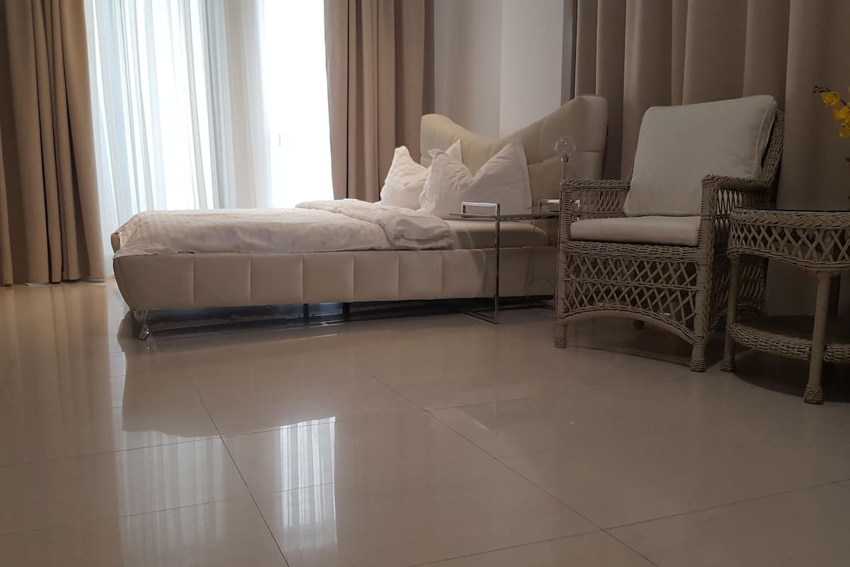 Un dormitorio moderno con una cama grande, una mesita de noche, una silla de mimbre y vistas al exterior a través de cortinas translúcidas.