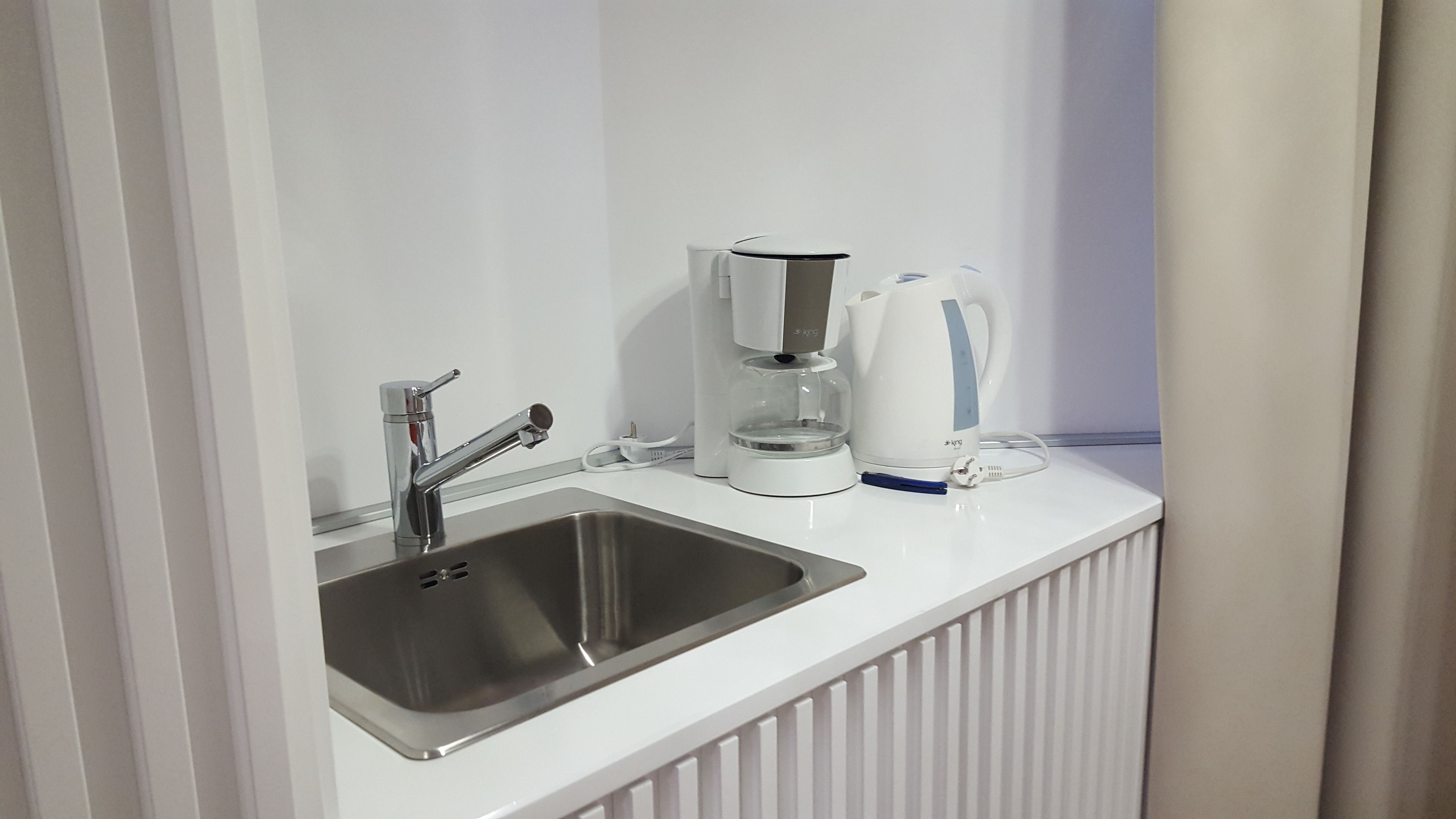 A modern kitchen with a stainless steel sink, a coffee maker, and a kettle on a white countertop.